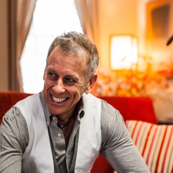 Joe Locke sits on a sofa and smiles to the side, hands clasped.