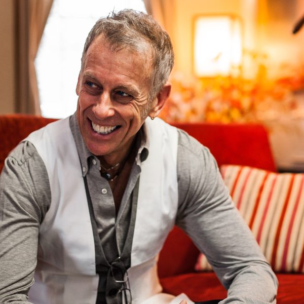 Joe Locke sits on a sofa and smiles to the side, hands clasped