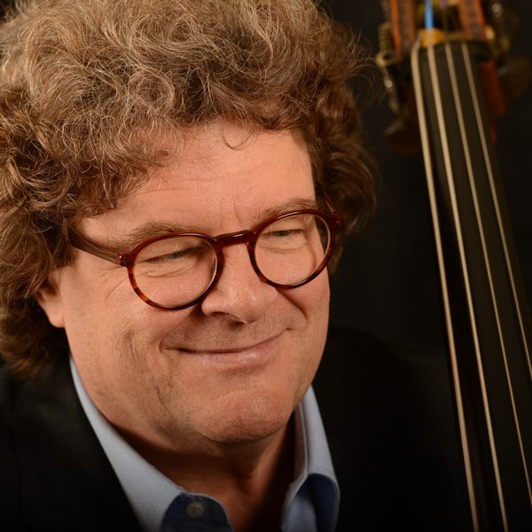 Head and shoulders shot of Joel Quarrington looking thoughtfully, with the neck of a double bass in the background