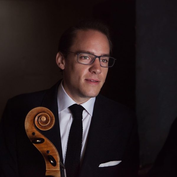 Portrait of a double bass player holding the neck of the instrument, looking off camera.