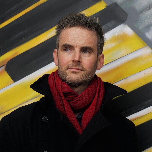 John Reid poses for headshot next to an outdoor painted mural.