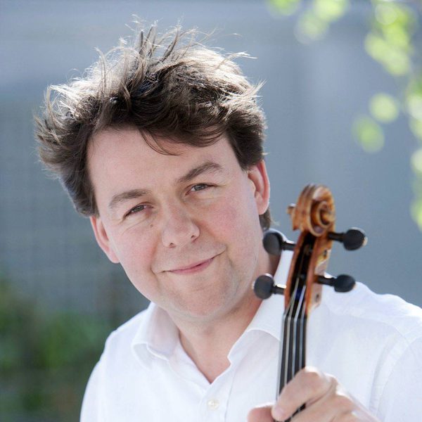 Jon thorne smiles to camera, holding violin.