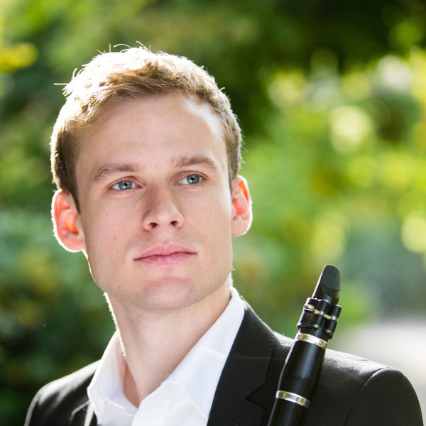 Jordan Black poses for camera holding a clarinet in a green outdoor setting.