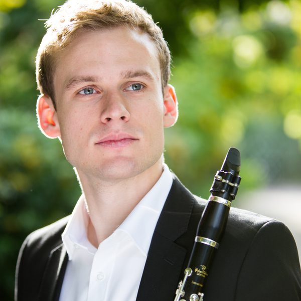 Jordan Black poses for camera holding a clarinet in a green outdoor setting.