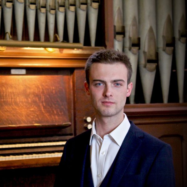 Joseph Beech smiles to camera in front of an organ.