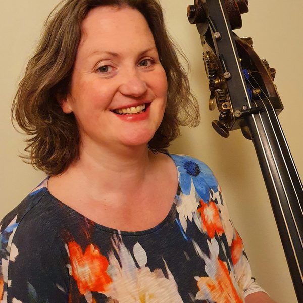 Josie Ellis smiles for camera, holding the neck of a double bass