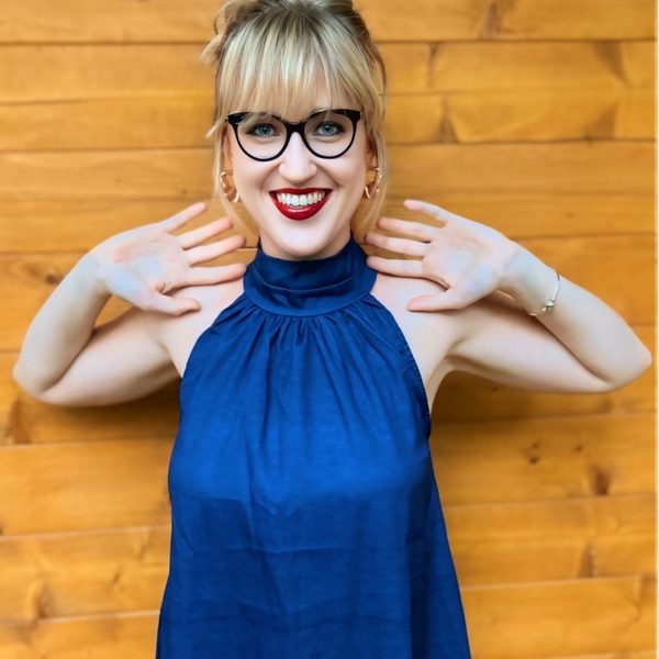 Julia Klimek stands against a wooden wall, smiling to camera in dark blue with elbows lifted.