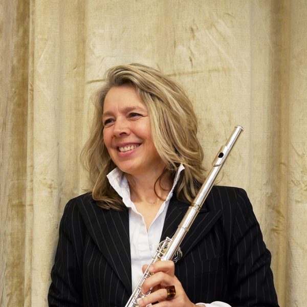 Karen Jones stands smiling and looking to the side while holding a flute.