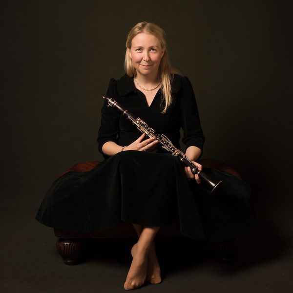 Katherin Spencer sits against a dark background holding a clarinet.