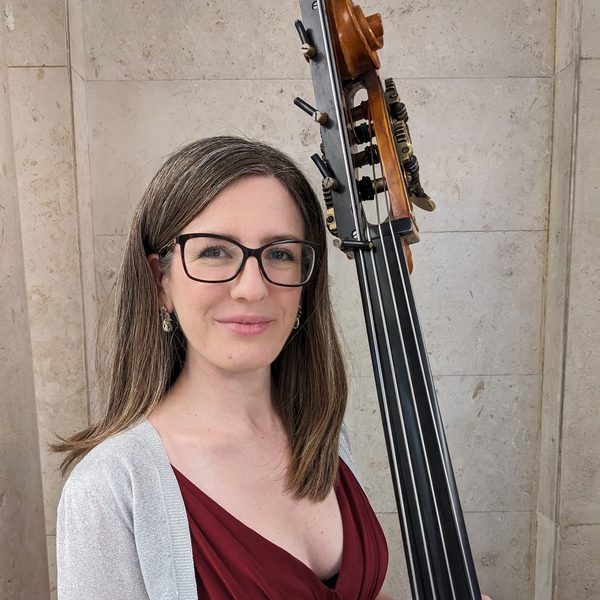 Portrait of Katy Furmanski smiling to camera, holding double bass.
