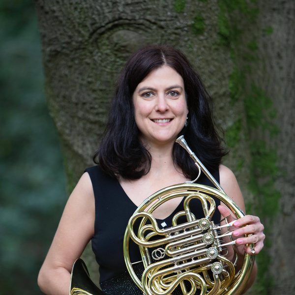 Kerin Black holds a horn, smiling to camera outside.