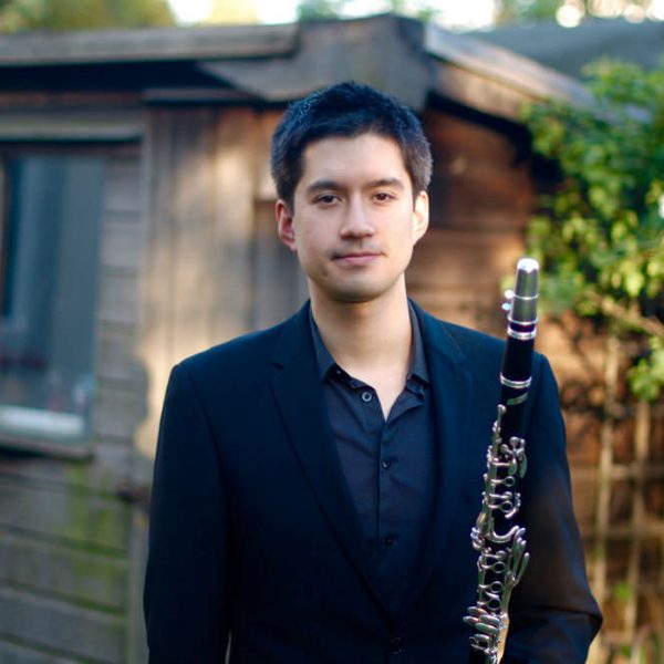 Kimon Parry smiles to camera, holding a clarinet outside.