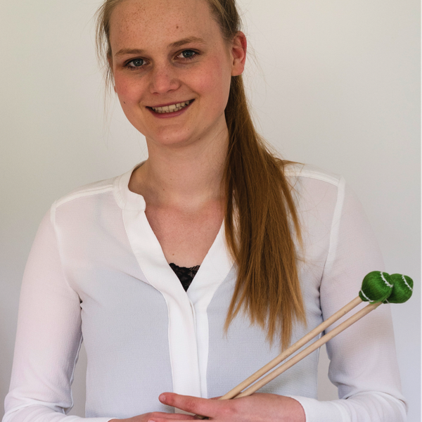 Kizzy stands posing for headshot against a plain white background, holding percussion mallets.