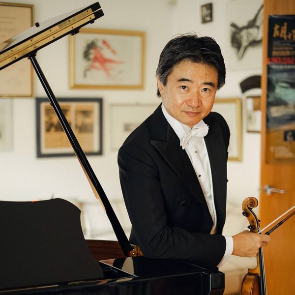 Kun Hu faces the camera, standing aside a piano.