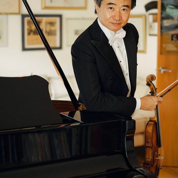 Kun Hu faces the camera, standing aside a piano.