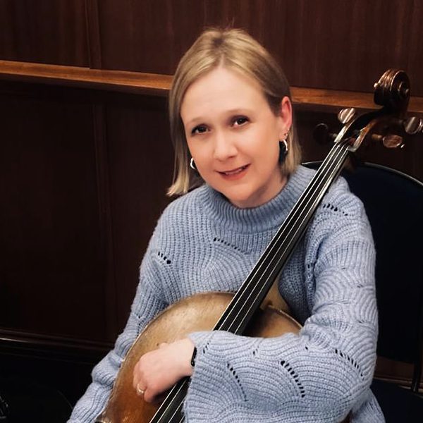 Lara Moore poses for camera, holding the neck of a cello.