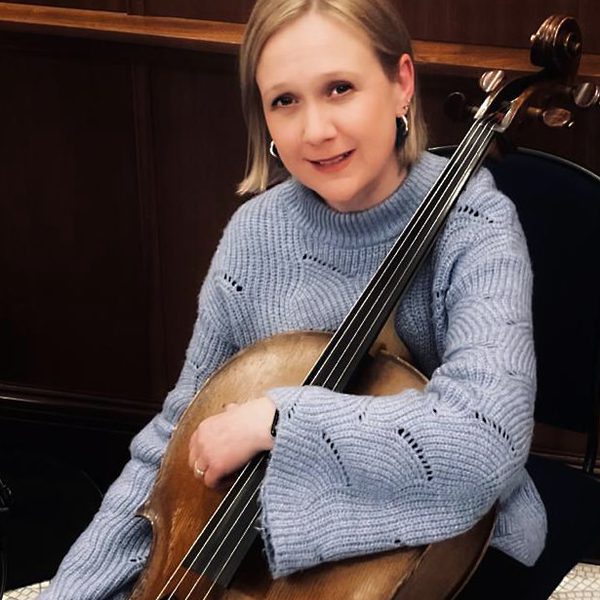 Lara Moore poses for camera, holding the neck of a cello.