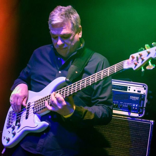 Laurence Cottle beneath stage lights, playing an electric bass guitar.