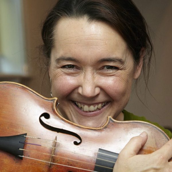 Portrait of Margaret Faultless smiling for camera, holding a violin across shoulders.