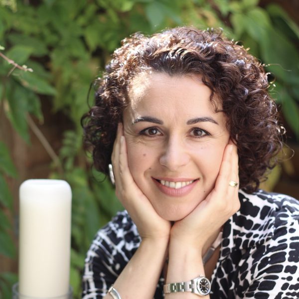 Marie Vassiliou smiles to camera with face cradled in hands.