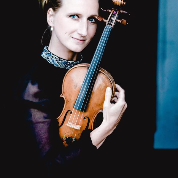 Marije Johnston looks to camera, holding violin.