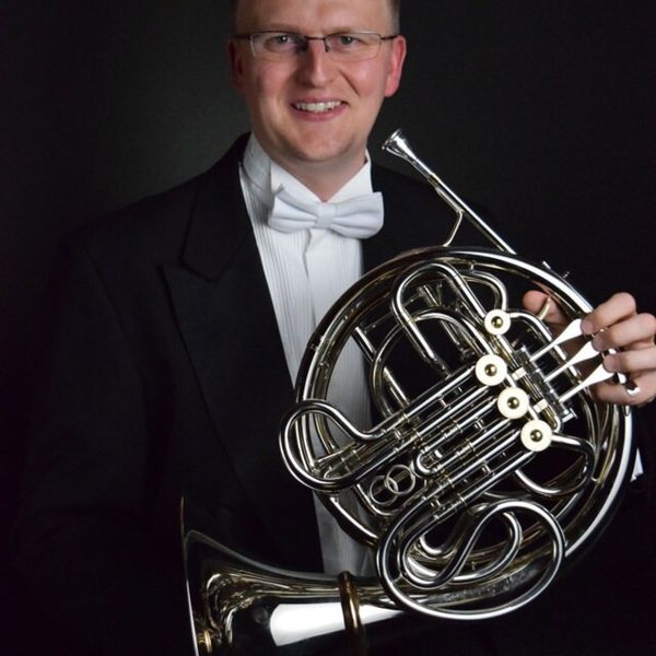 Mark Almond smiles to camera holding a horn.
