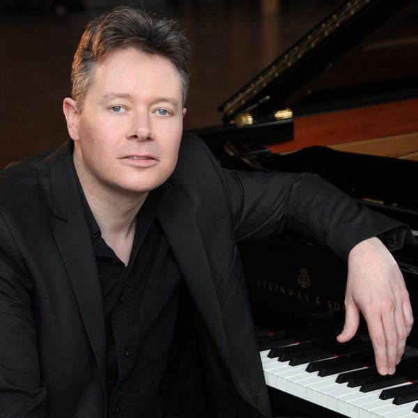 Mark Nixon sits at a piano keyboard, posing for camera.