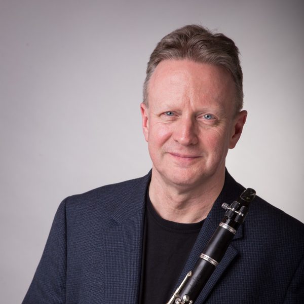 Mark van de Wiel holds a clarinet, smiling to camera.