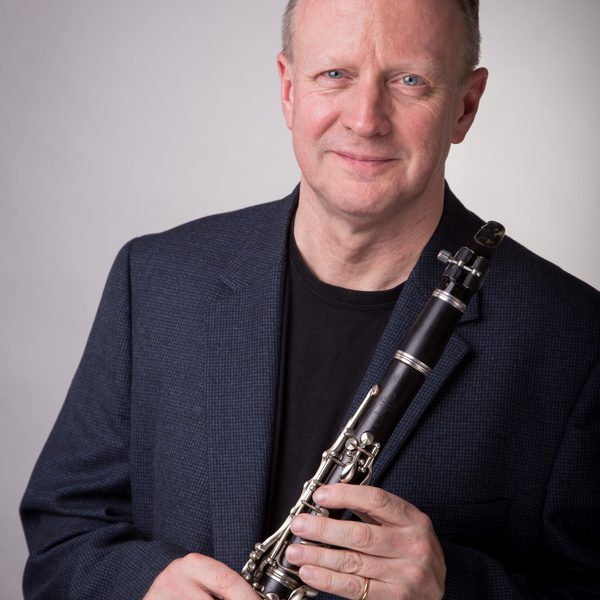 Mark van de Wiel holds a clarinet, smiling to camera.