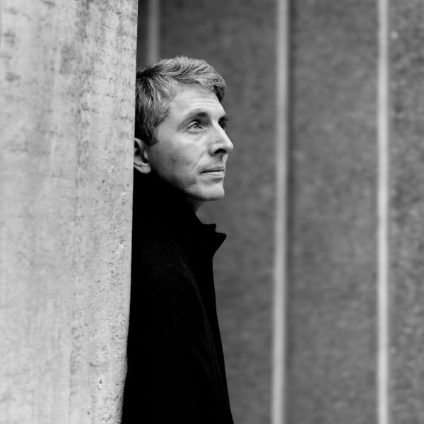Christian Mason emerges in profile from behind a wall, in black and white