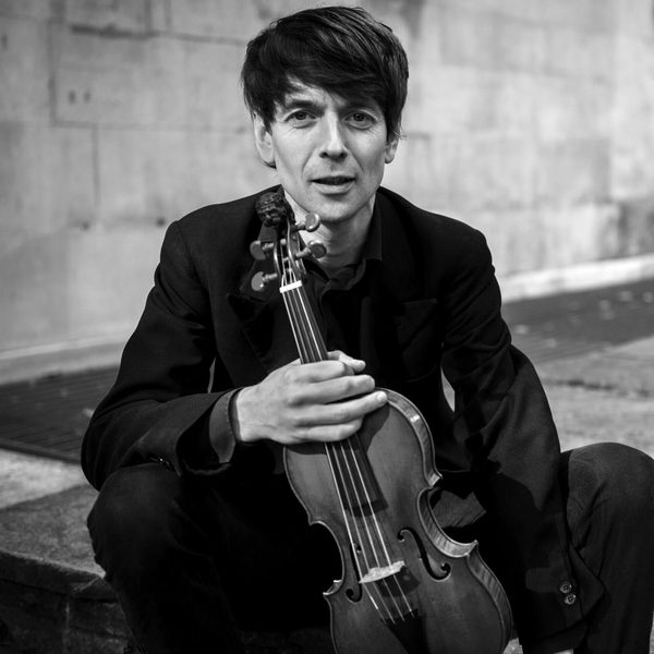 Matthew Truscott sits on the ground holding a violin.