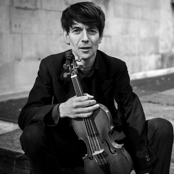 Matthew Truscott sits on the ground holding a violin.