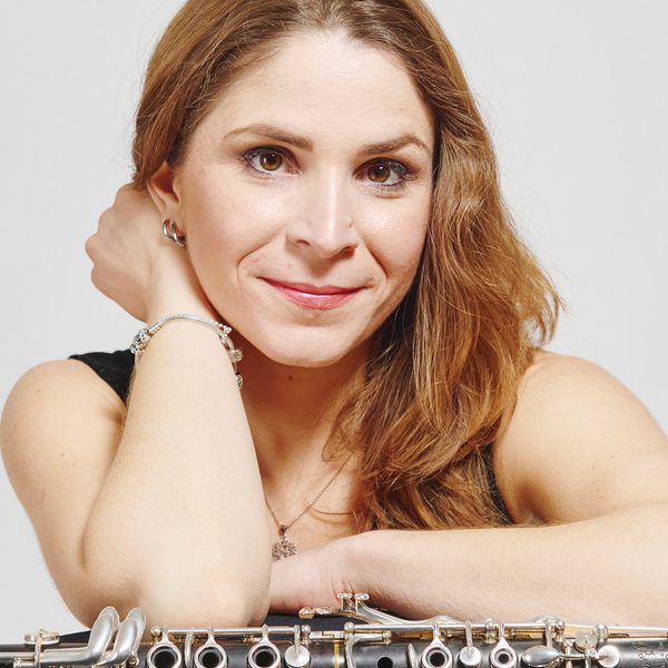 Portrait of Maura Manucci looking to camera, leaning over a clarinet placed flat across a surface.