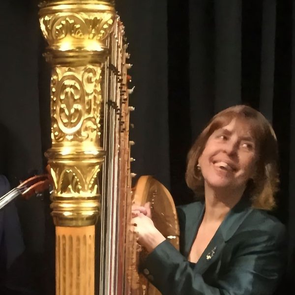 Miriam Keogh stands at a harp, smiling.