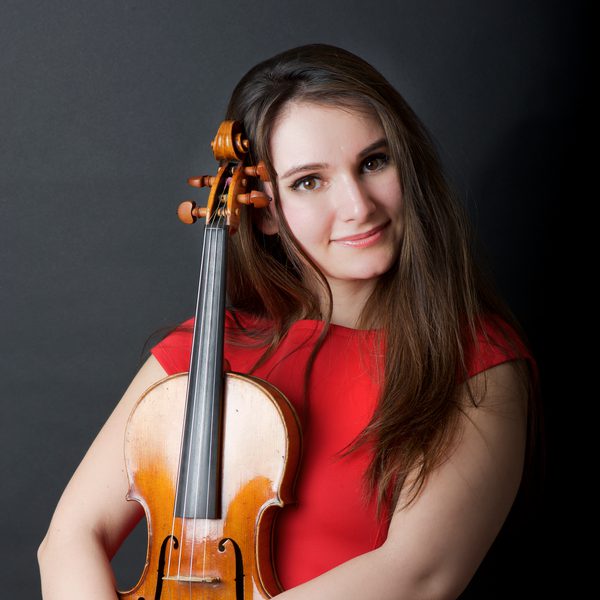 Nazrin Rashidova holds a violin, smiling to camera in a red dress.