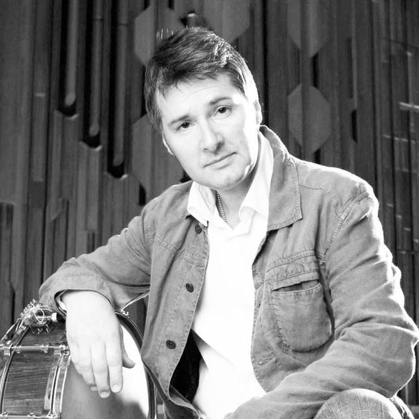 Portrait of Neil Percy smiling to camera, leaning on a snare drum turned on its side.