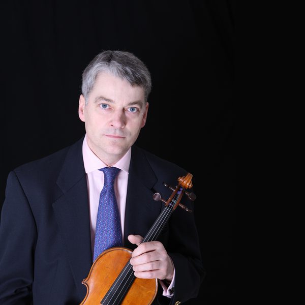 Nicholas Miller looks to camera, holding violin.