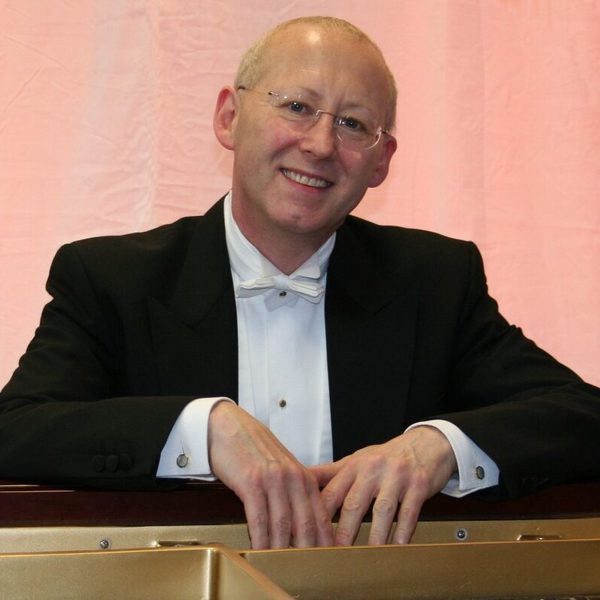 Nicholas Walker smiles to camera while leaning on a railing with a pastel pink material background
