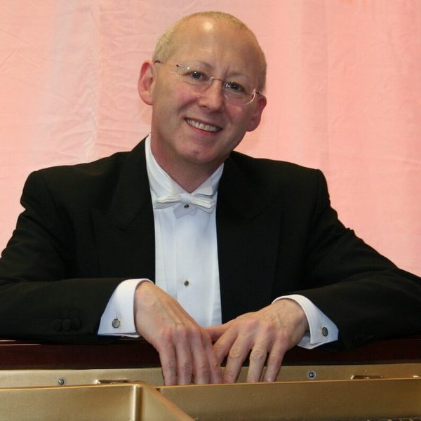 Nicholas Walker smiles to camera while leaning on a railing with a pastel pink material background.