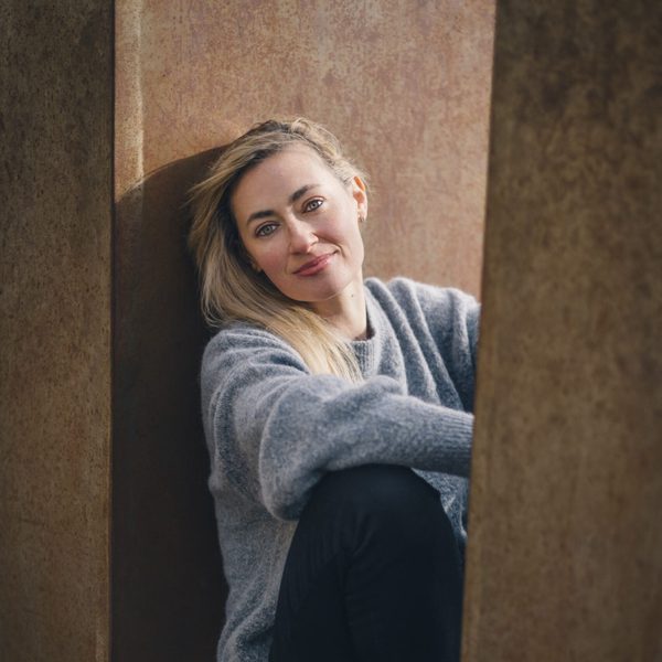 Nicola Eimer sits on a ledge outside, posing for headshot, facing camera.