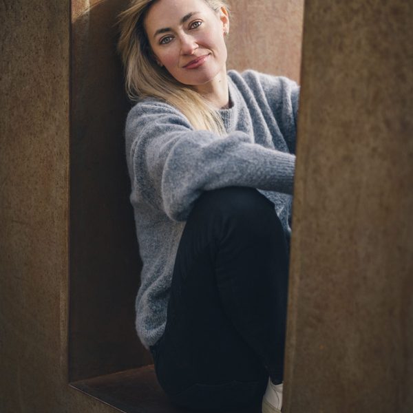 Nicola Eimer sits on a ledge outside, posing for headshot, facing camera.