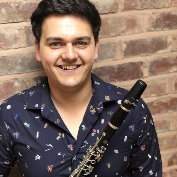 Oliver Janes smiles to camera, holding clarinet.