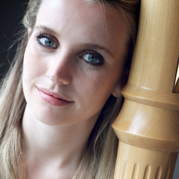 Olivia Jageurs looks to camera, next to a harp.