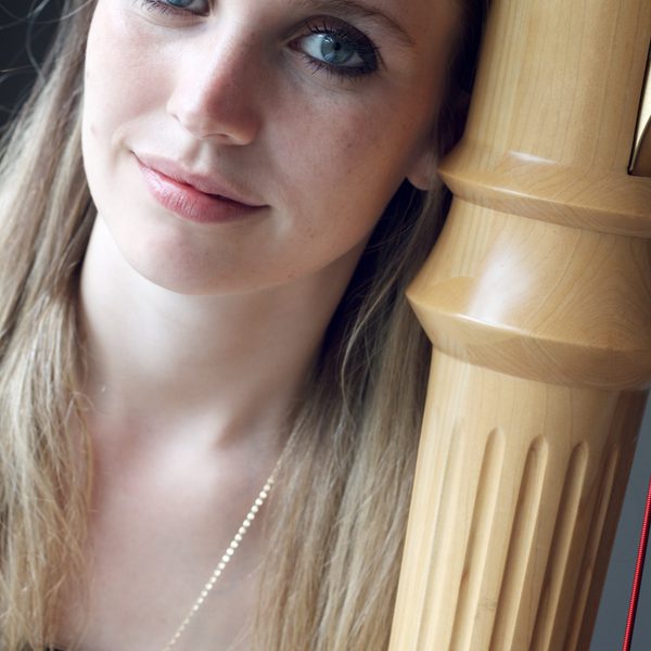 Olivia Jageurs looks to camera, next to a harp.