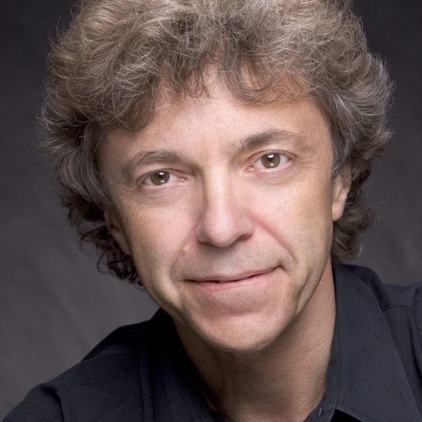 A headshot of Pascal Roge smiling to camera with a dark backdrop.