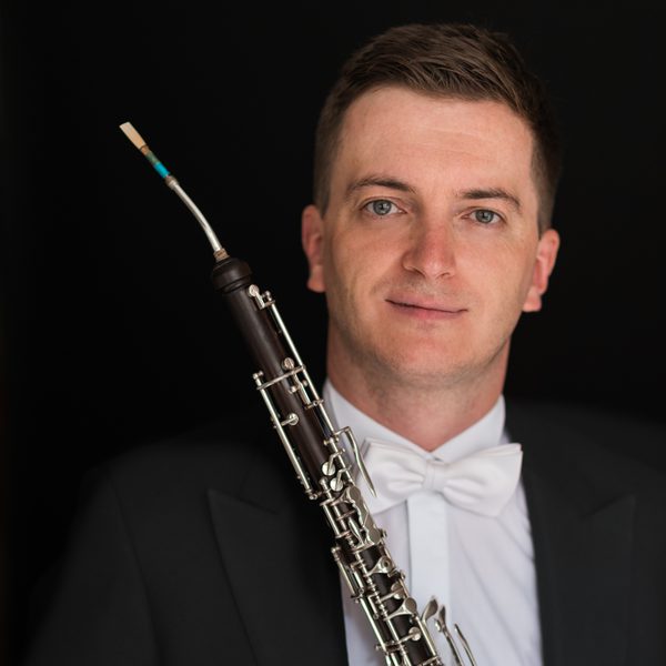 Patrick Flanaghan poses in a tuxedo holding a Cor Anglais abreast.