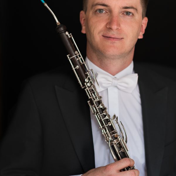 Patrick Flanaghan poses in a tuxedo holding a Cor Anglais abreast.