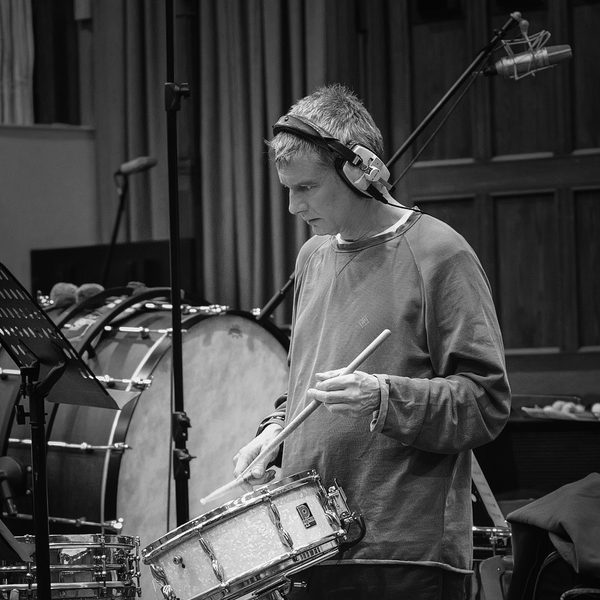 Paul Clarvis wears headphones and plays a snare drum.