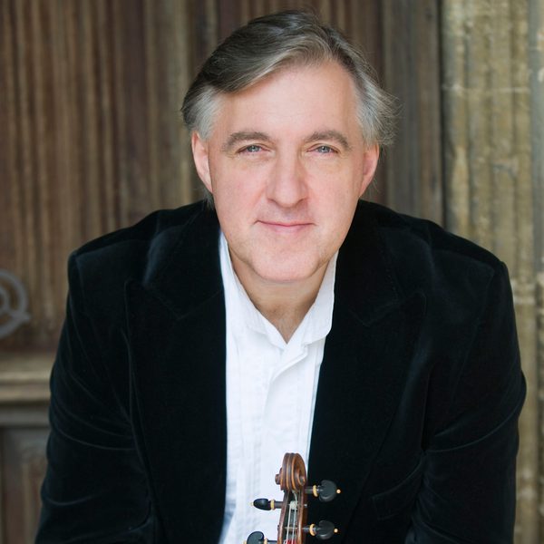 Pavlo Beznosiuk Headshotholds a violin at the neck with both hands, smiling to camera.