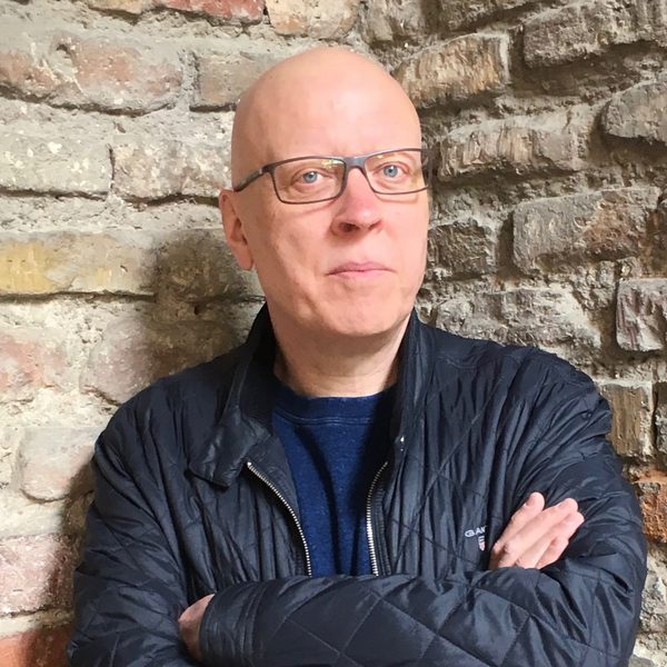 Phil Cashian looks to camera, with arms folded against a brick wall.
